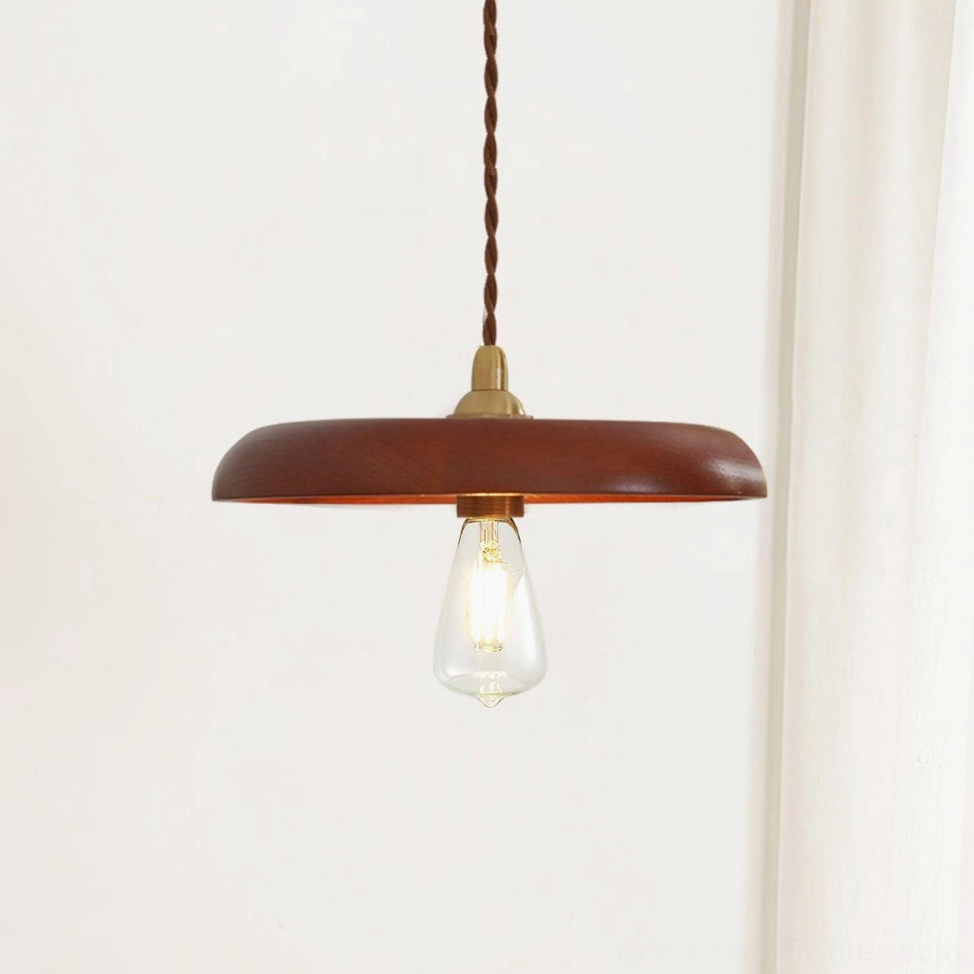 Three-quarter view of wood disc pendant lamp showing twisted brown fabric cord and polished brass socket