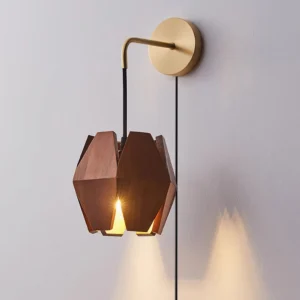 Geometric wood wall lamp illuminated with warm ambient light, front close-up view on light gray indoor wall, displaying dark walnut wood and brass hardware