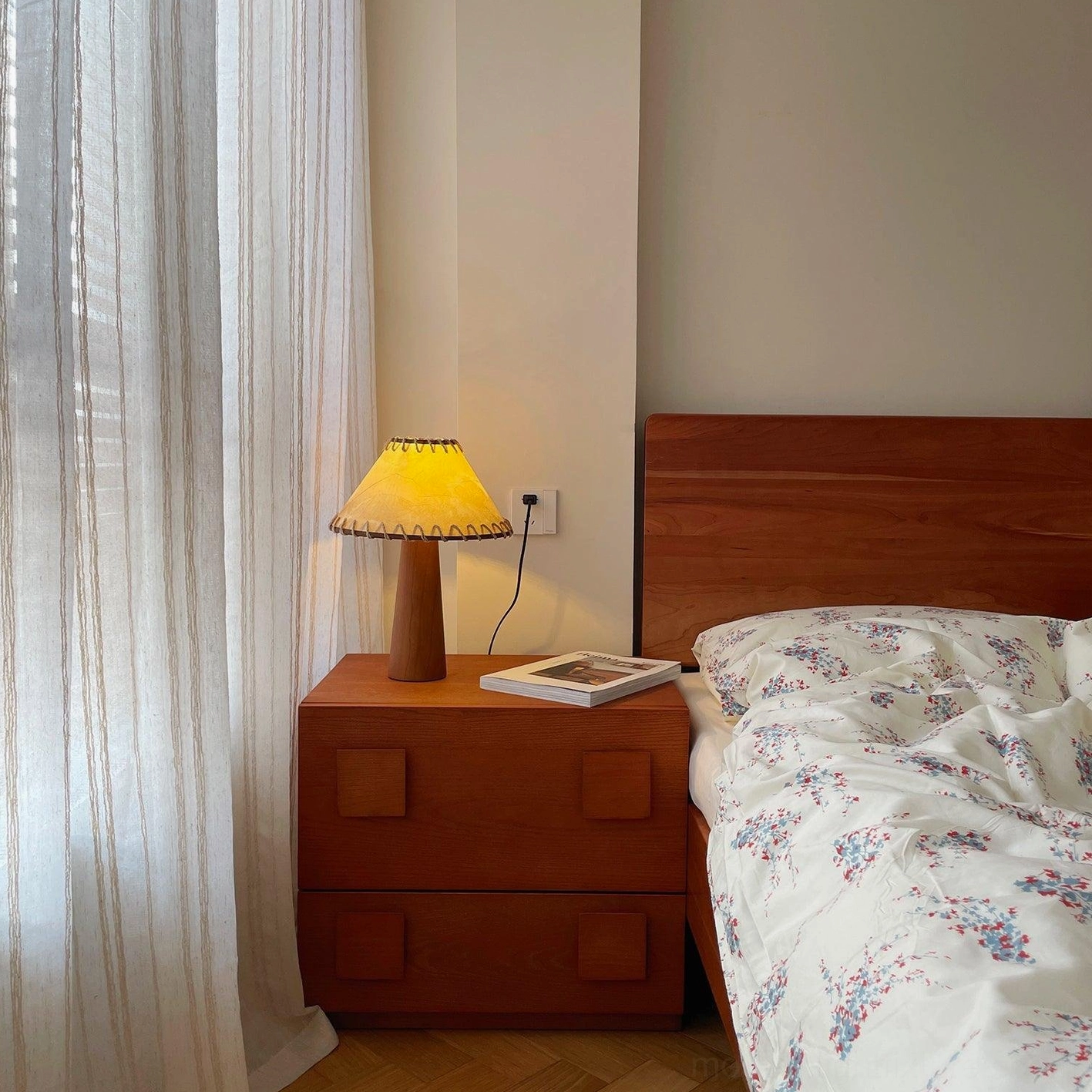 Wood base table lamp in bedroom setting on nightstand with mid-century modern decor and warm lighting ambiance