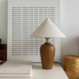 Wooden table lamp with brass metal connector displayed in bedroom nightstand scene with warm ambient lighting