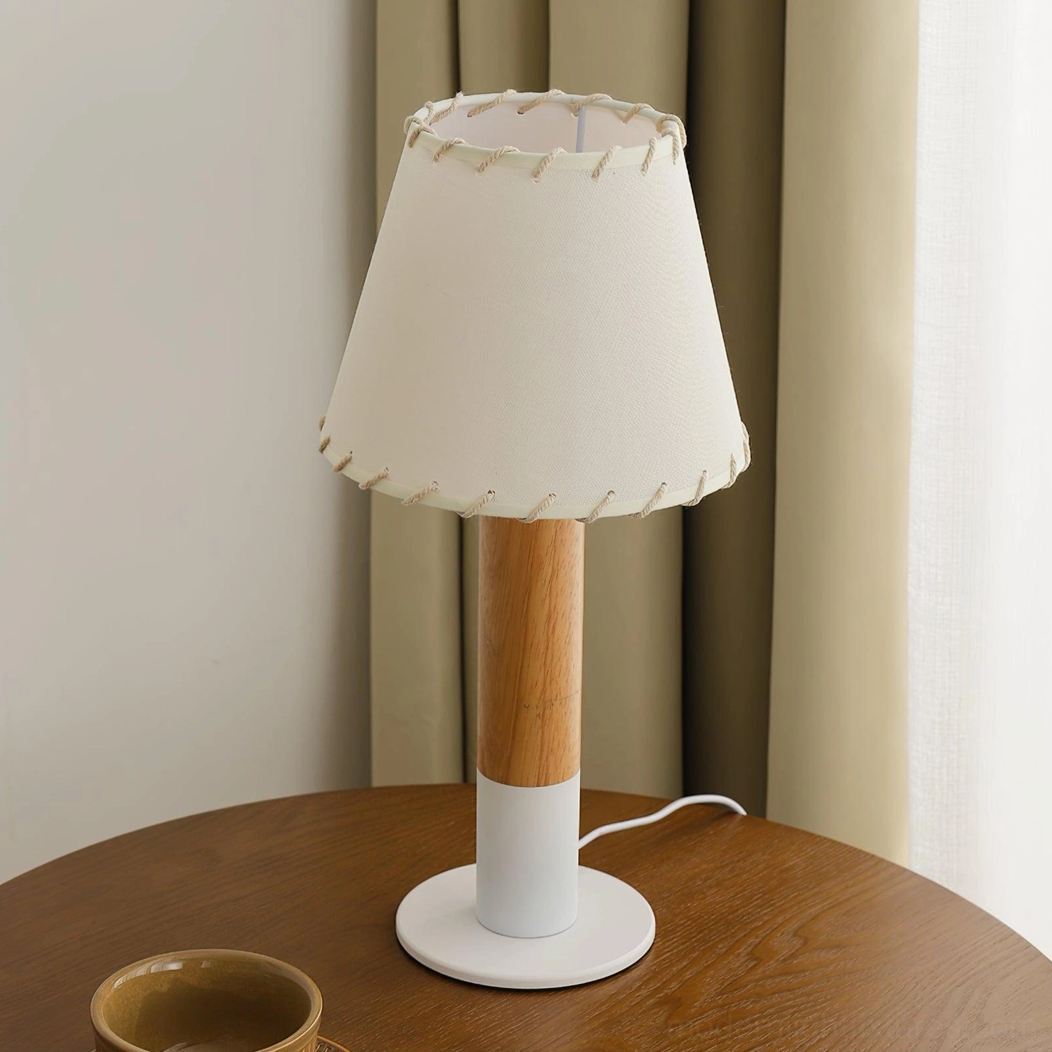 Natural rubber wood table lamp with white round fabric base side view against window backdrop