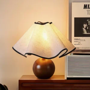Modern wood table lamp with warm glowing curved fabric shade and brown spherical wooden base, three-quarter angle on side table