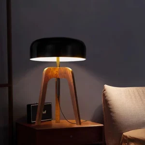 Wood tripod table lamp illuminated in bedroom nightstand setting with warm ambient lighting and bedside décor, three-quarter view