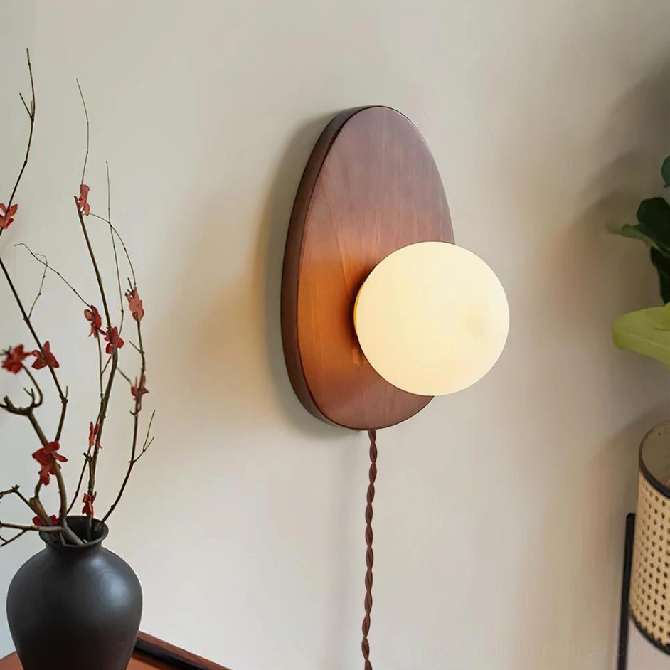 Brown wooden oval wall sconce with illuminated frosted glass shade in corner setting with red floral decor