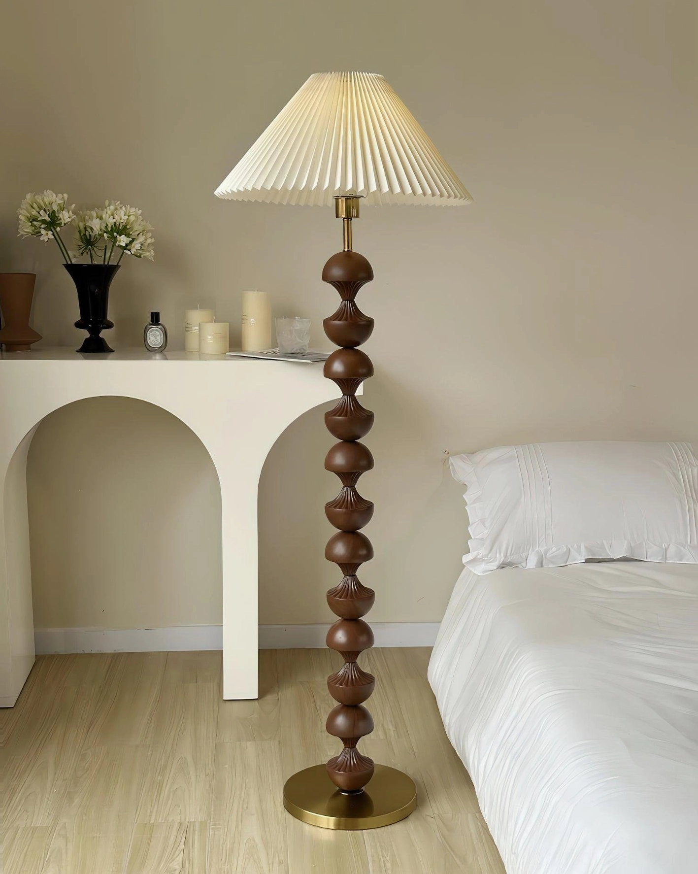 Pleated shade wooden beaded floor lamp eye-level oblique view in bedroom with arched console table, dark brown wood pole, brass metal base