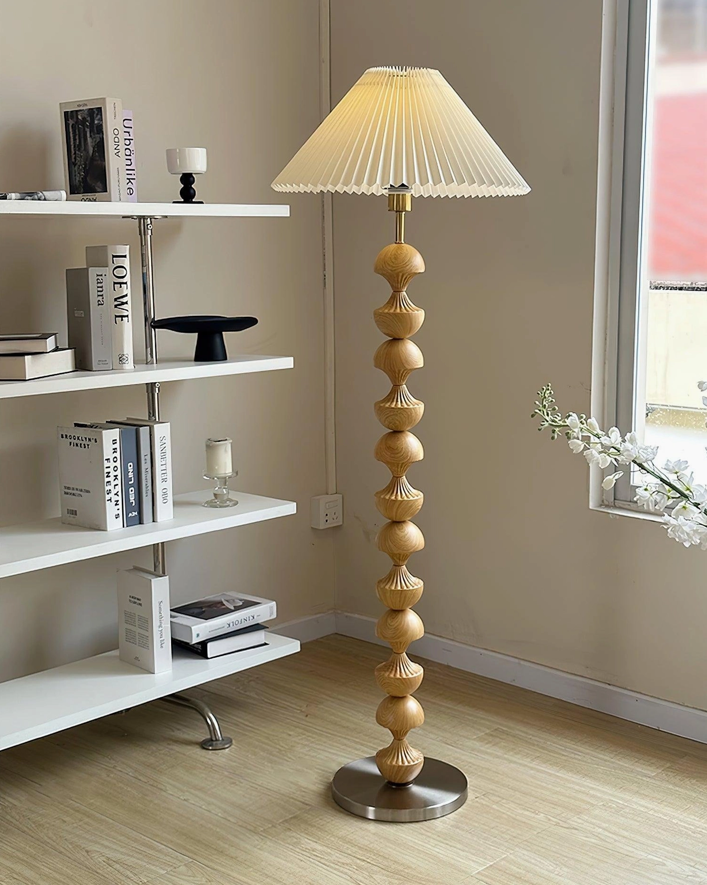 Light wood grain beaded floor lamp wide oblique view in living room with bookshelf and decorative flowers, silver metal base, warm home interior