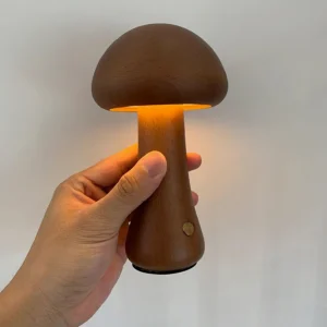 Wooden mushroom lamp close-up side view with hand holding, illuminated warm LED light and brass touch control button