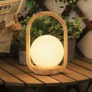 Three-quarter front view of wooden table lamp outdoors on patio with warm ambient lighting and potted plants