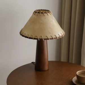 Wooden table lamp with textured jute shade on side table, three-quarter angle showing craftsmanship details and warm wood tone