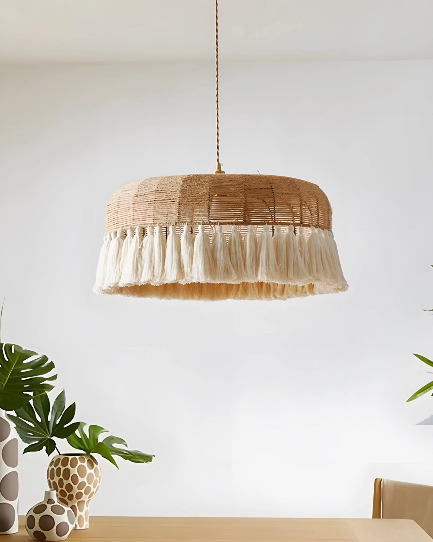 Artisan woven rattan drum pendant light suspended above dining table with decorative plants, bohemian interior styling