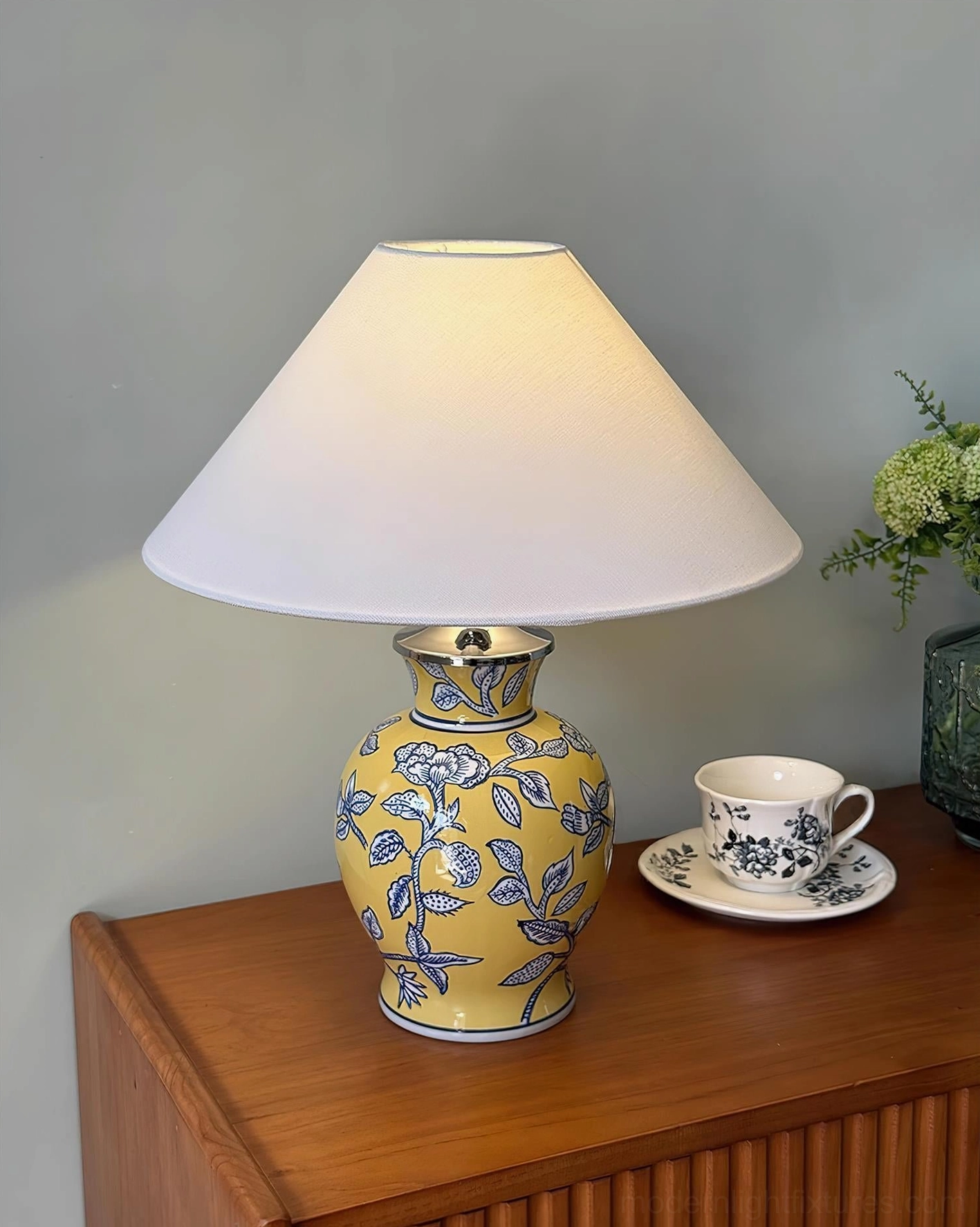 Yellow ceramic floral table lamp with blue botanical motifs, side table with coffee set and green plant decor