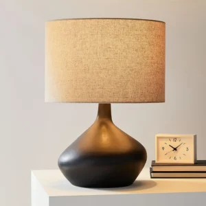 Modern minimalist table lamp with dark brown ceramic base and tan woven fabric shade on decorative desk display
