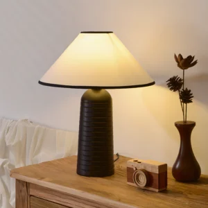 Modern minimalist table lamp with tapered shade and hand-tooled textured base, three-quarter perspective on bedside dresser