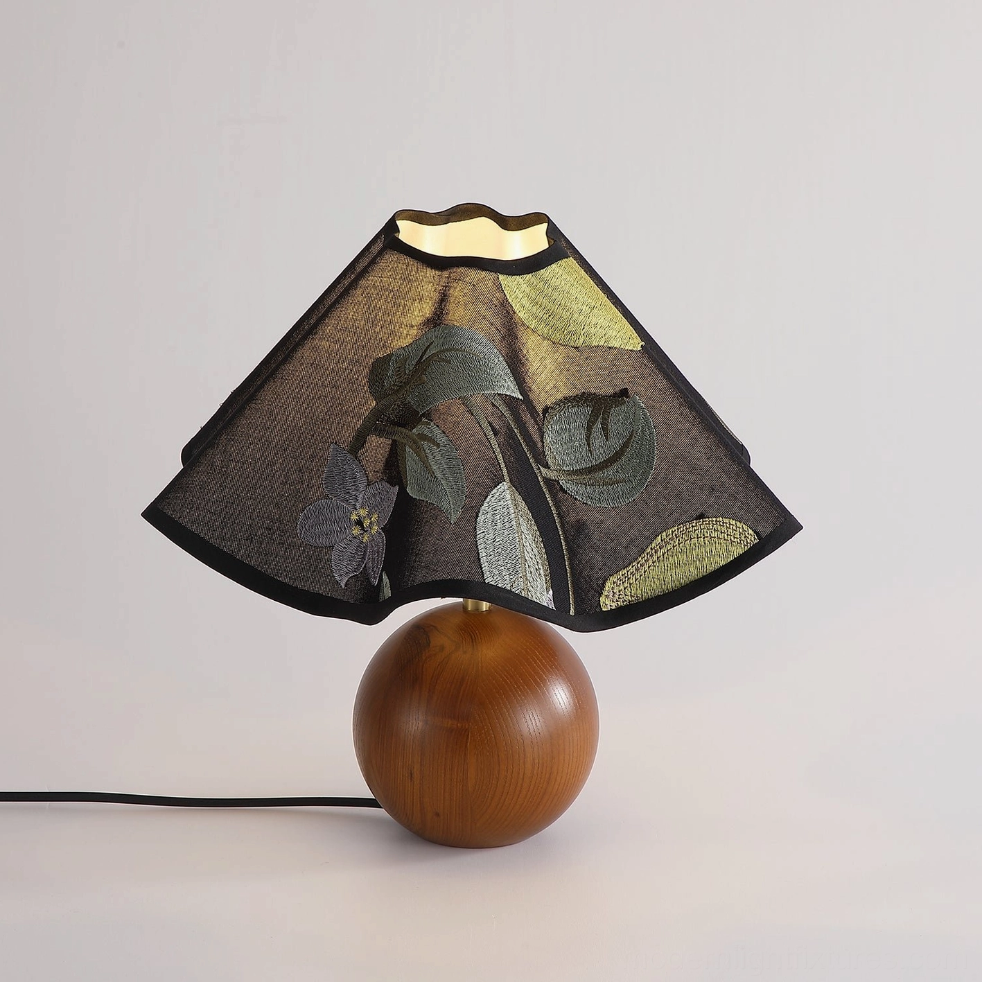 Zerina table lamp backlit view highlighting embroidered fabric shade design and wooden sphere base